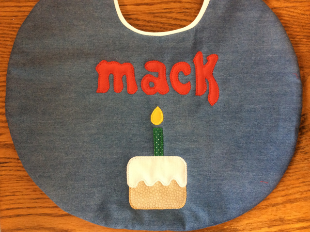 10" round birthday bib, first name only, with cake and candle under name shown here in medium denim 