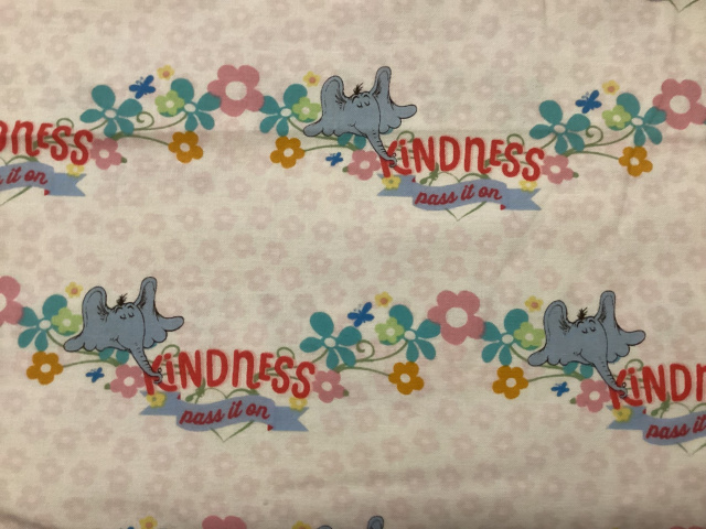 a blue elephant on a soft pink floral background with its trunk around the word kindness